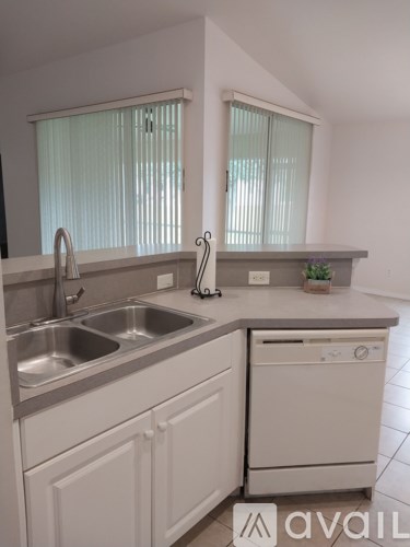 A kitchen with a sink, dishwasher, and a window with blinds.
