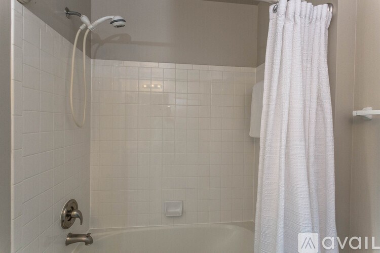 A white shower curtain hangs in a white tiled shower.