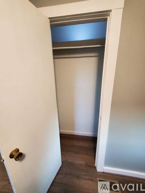 A white door with a brass handle is open to a room with a wooden floor.
