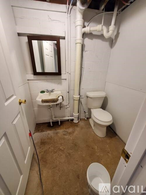 A bathroom with a toilet, sink, and a pipe running along the wall.