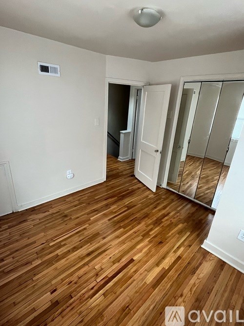 A room with wooden flooring and a white wall with a doorway leading to another room.