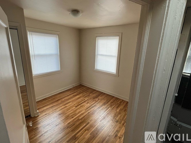 A room with wooden flooring and two windows.