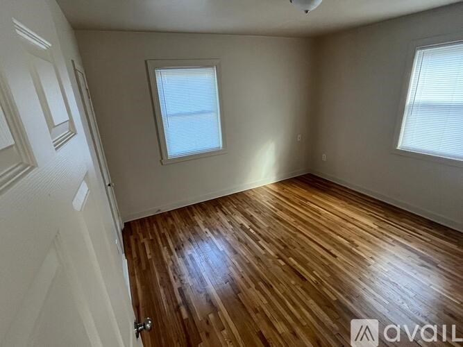 A room with wooden flooring and two windows.