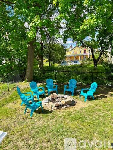 A set of blue chairs are arranged around a fire pit in a yard.