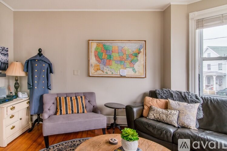 A living room with a grey couch, a purple chair, a wooden dresser, a small table, a plant, and a framed map of the United States on the wall.