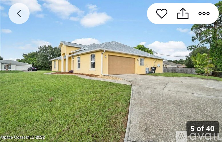 A yellow house with a grey roof is surrounded by a green lawn.