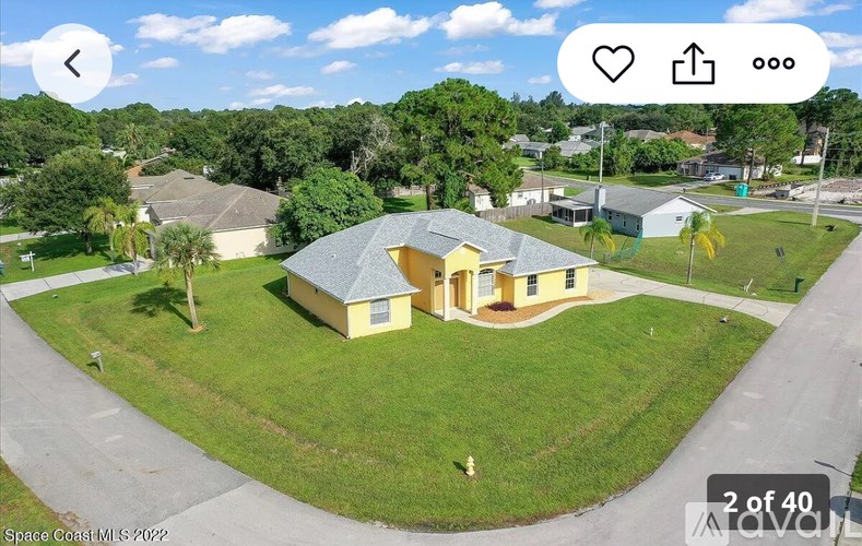 A yellow house with a grey roof is surrounded by a green lawn and trees.