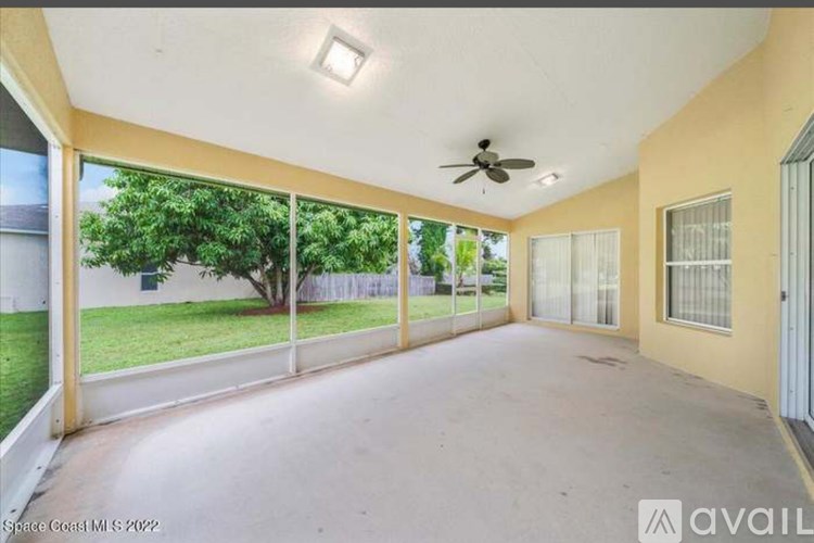 A spacious room with a ceiling fan and sliding glass doors leading to a green outdoor area.