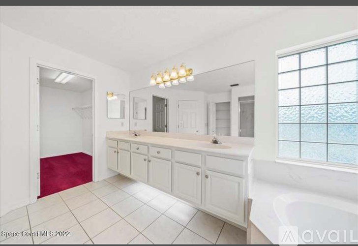 A white bathroom with a red rug and a window.