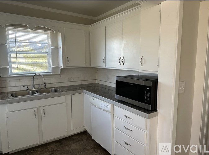 A kitchen with white cabinets and a black microwave.