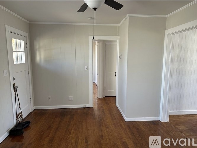 A room with wooden floors and white walls, with a ceiling fan and a broom leaning against the wall.