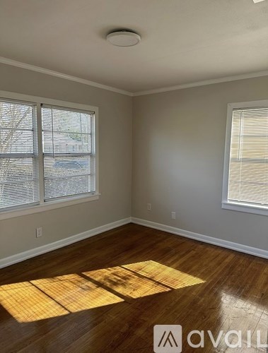 A room with wooden floors and two windows with blinds.