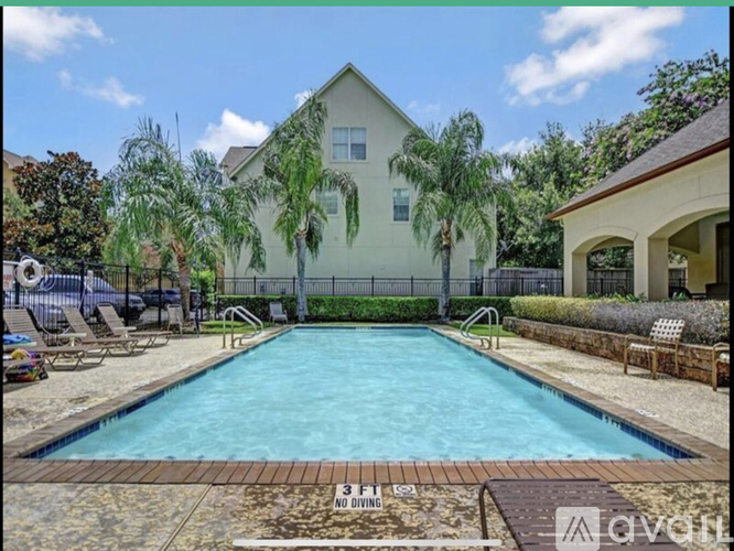 A pool surrounded by a fence and a house with a tree in front of it.