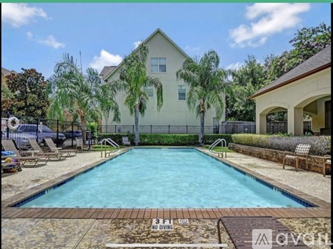 A pool surrounded by a fence and a house with a tree in front of it.