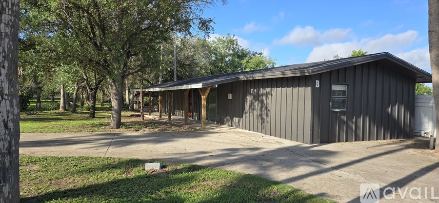 A grey building with a porch and a sign that says "available" in the front yard.