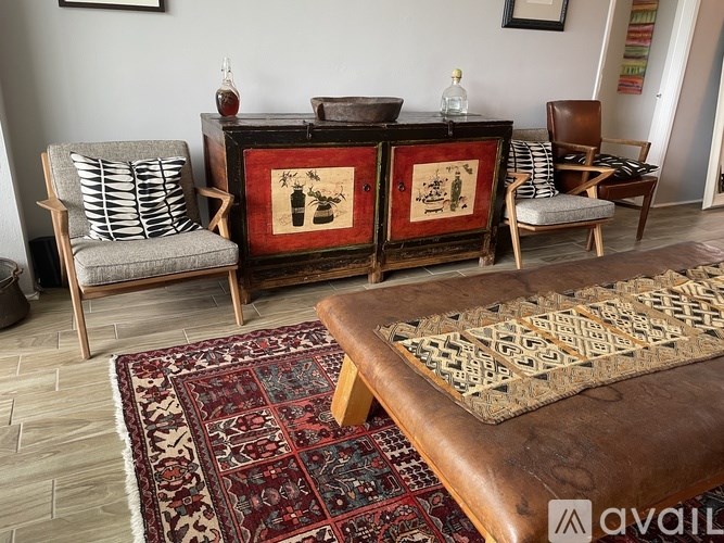 A room with a rug, a wooden cabinet, and two chairs.