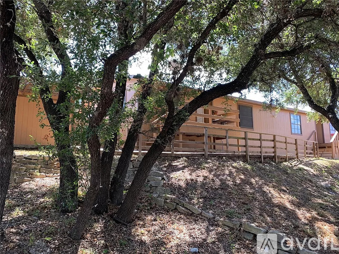 A house is surrounded by trees and has a stone wall in front.