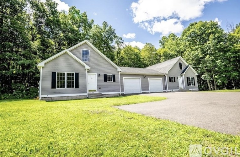 A two-story house with a garage is surrounded by greenery.
