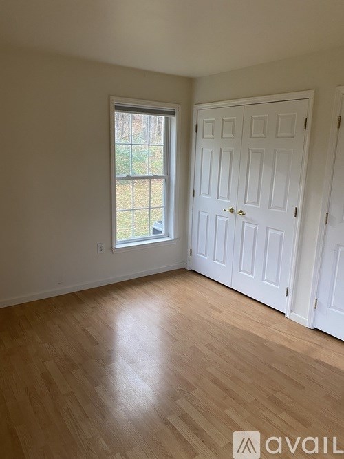 A room with a white door and a window with a view of a fence and trees.