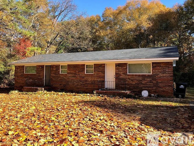A small house with a white door and windows surrounded by fallen leaves.