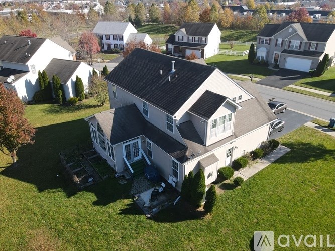 A large house with a black roof is surrounded by smaller houses and trees.