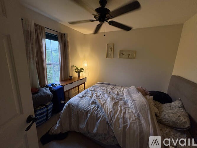 A bedroom with a bed, a ceiling fan, and a window with curtains.