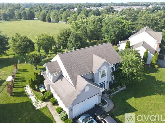 A large house with a grey roof is surrounded by a green lawn and trees.