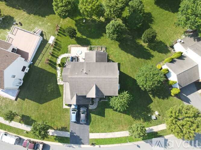 A house with a driveway and a car is surrounded by green grass and trees.