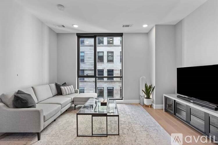 A modern living room with a grey sofa, a glass coffee table, and a flat-screen TV.