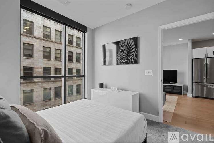 A bedroom with a large bed, a television, and a large window overlooking a building.