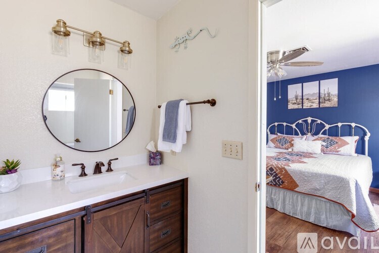 A bathroom with a round mirror and a bedroom in the background.