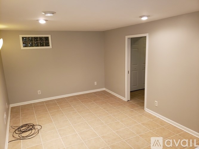 A room with beige walls and tile flooring, with a doorway leading to another room.