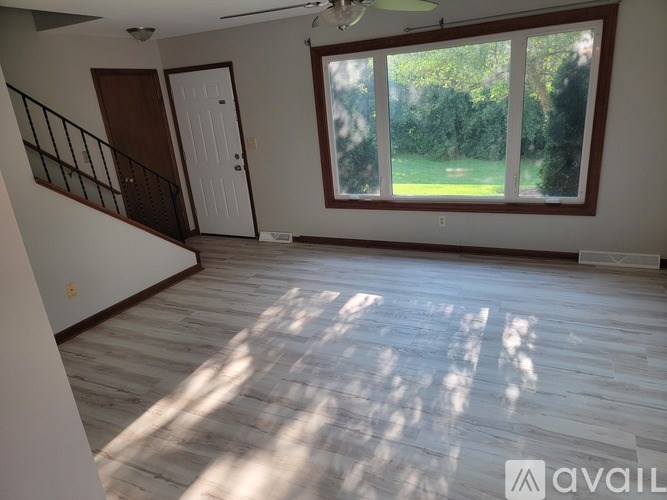A room with wooden flooring and a large window overlooking a green lawn.