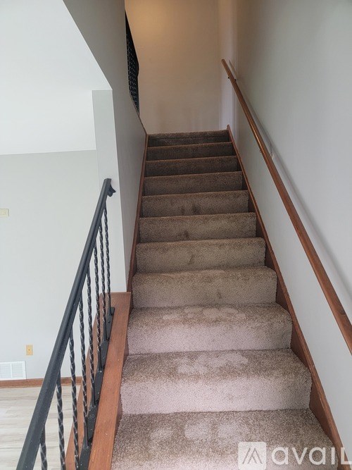 A staircase with a beige carpeted runner and a black railing.