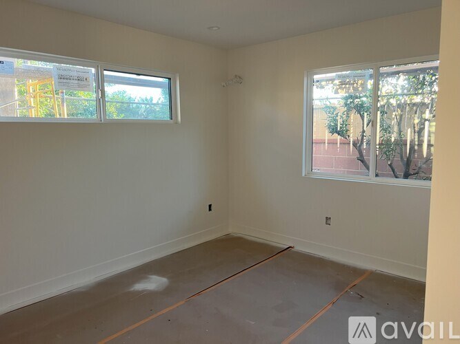 A room with two windows and a floor that is half painted.