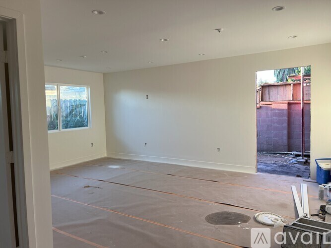 A room with a white wall and a window with a view of a fence and trees.