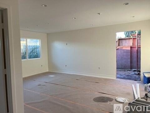 A room with a white wall and a window with a view of a fence and trees.