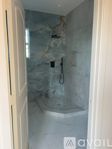 A bathroom with a marble shower and tiled floor.