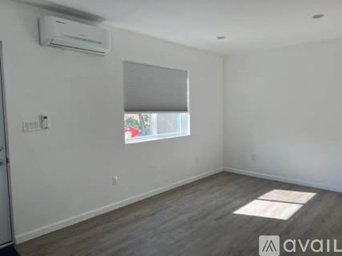 A room with a window covered by a white blind and a wooden floor.