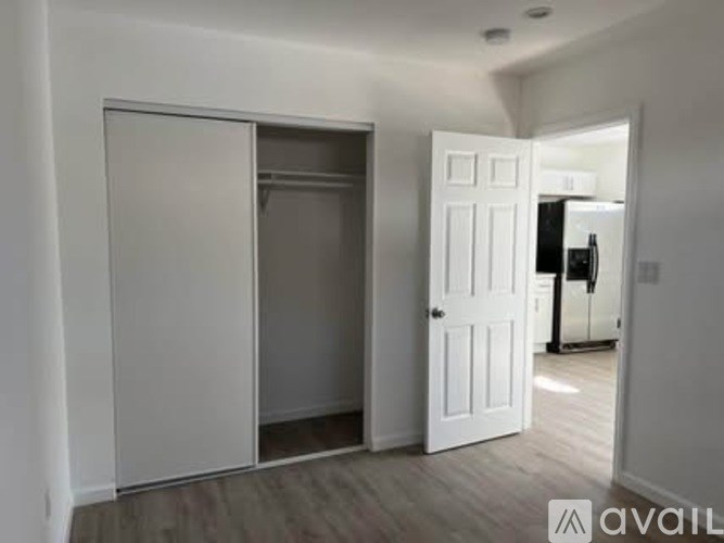 A white door is open to reveal a room with a black refrigerator.