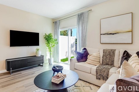 A living room with a black sofa, a coffee table, and a flat screen TV mounted on the wall.