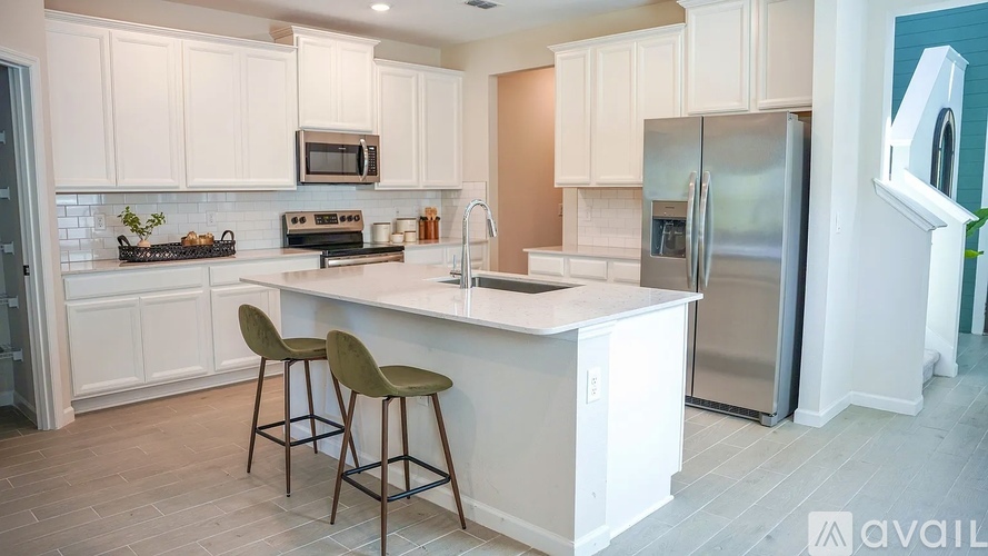 A kitchen with white cabinets and a white island with two chairs.