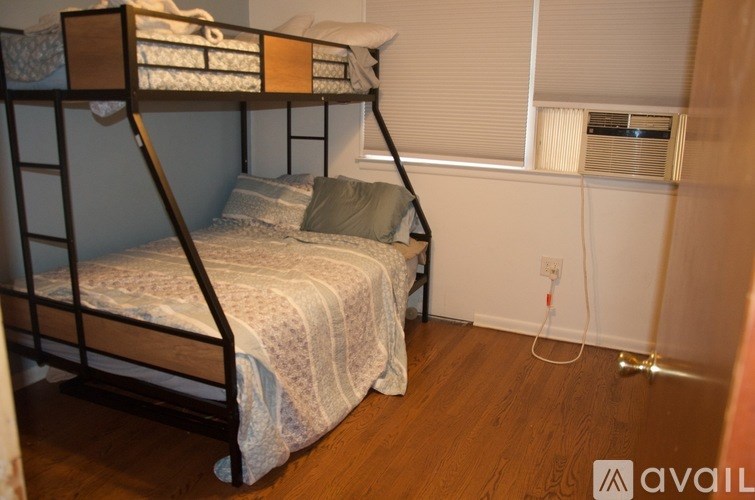 A bunk bed with a white blanket and pillow is in a room with wooden floors and a window with blinds.