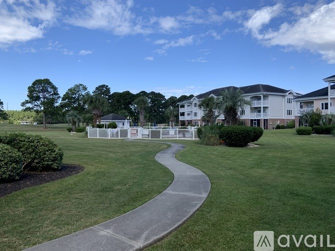 A pathway leads through a grassy area with a row of houses in the background.