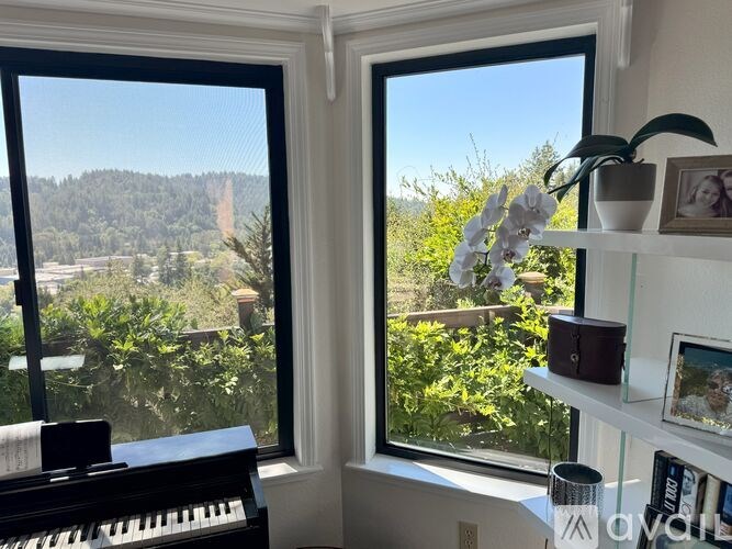 A room with a piano and a view of a garden through the window.