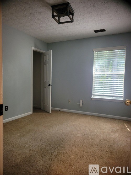 A room with a carpeted floor, a door, and a window with blinds.