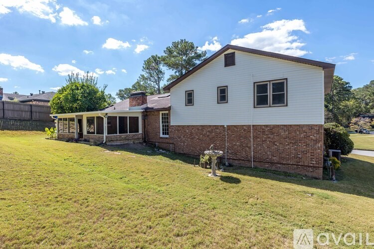 A house with a white exterior and a brick wall is surrounded by a grassy area.