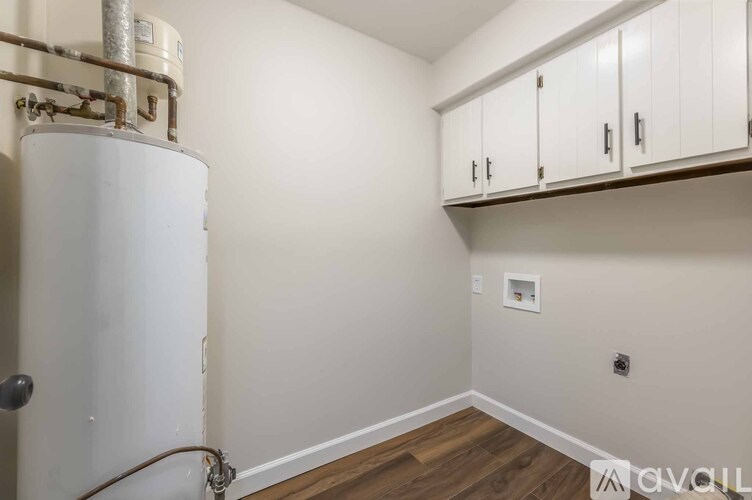 A white tank with pipes is next to a wall with a shelf above it.