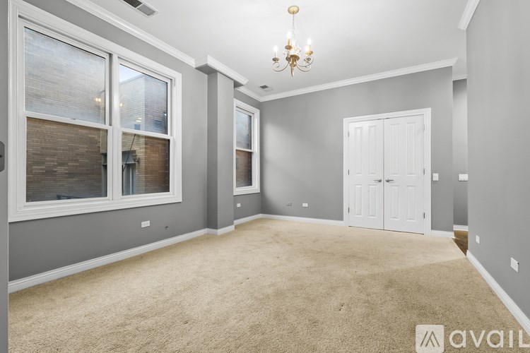 A spacious room with a chandelier, two windows, and a carpeted floor.