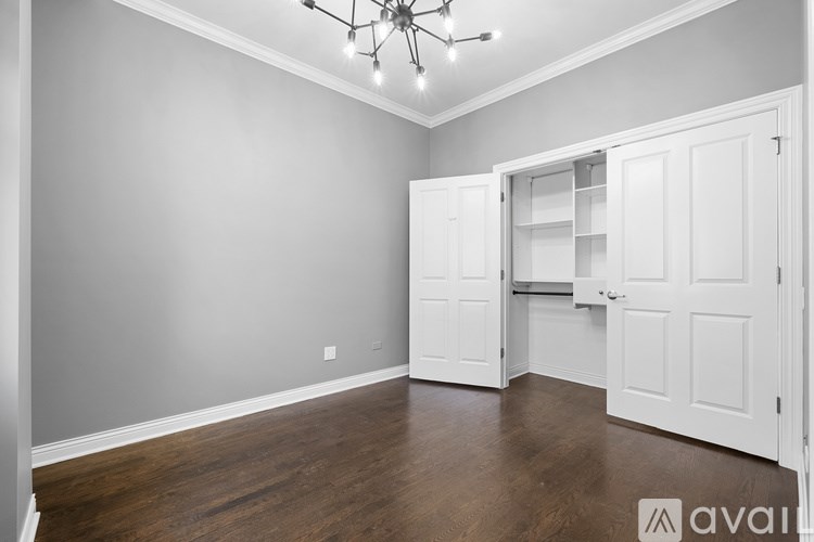 A room with a chandelier, wooden floors, and white walls with a door open to a closet.